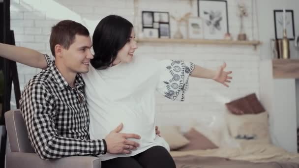 Ciężarna młoda kobieta siedzi na kolanach mąż przytula uruchomiony syn — Wideo stockowe