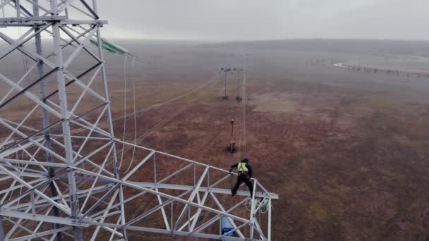Человек работает на электропередающей башне с проводами в поле — стоковое видео