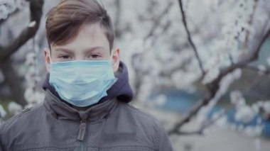 Gelişmekte olan bir ağacın arka planında tıbbi maskeli bir genç..