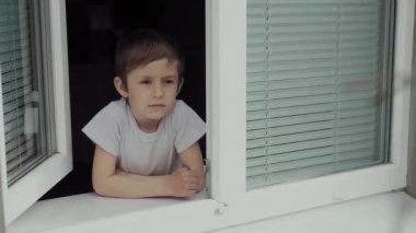 5 yaşında bir çocuk pencerenin önünde tek başına panjurlarla bekliyor..