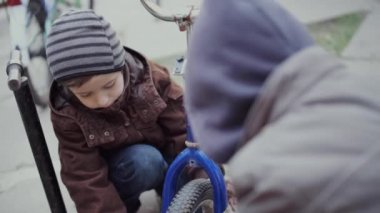 Ağabeyi, küçük kardeşine bisikleti pompalaması için yardım eder..
