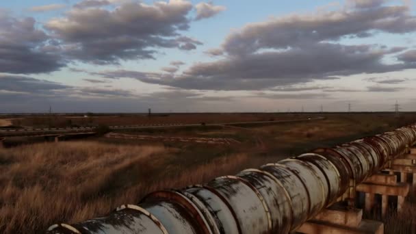 Autopista desierta con un coche solitario y una vieja tubería de agua de metal en un atardecer y un río pantanoso — Vídeo de stock