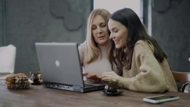 Bir kız, annesine online alışveriş için dizüstü bilgisayar kullanmayı öğretiyor..