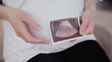 Hamile kadın elinde karnına yakın bir ultrason muayenesinin sonuçlarını tutuyor.