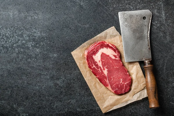 Raw ribeye steak and butcher knife on black board