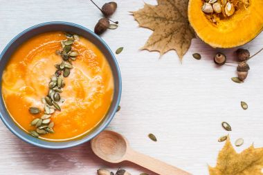 Beyaz ahşap bir masa üzerinde krem ve kabak çekirdeği kabak çorbası. Üstten Görünüm.