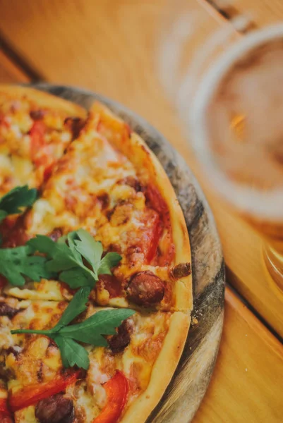 Sabrosa pizza y un vaso de cerveza están en la mesa de madera — Foto de Stock