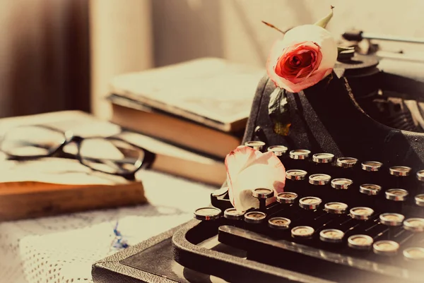 Máquina de escribir vintage con rosa rosa, libros antiguos en la mesa . — Foto de Stock