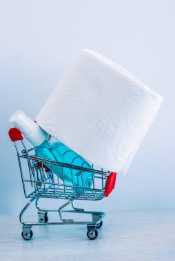 Tüketicilerin koronavirüs paniğinin sembolü olarak alışveriş arabasında beyaz tuvalet kağıdı ve dezenfektan.