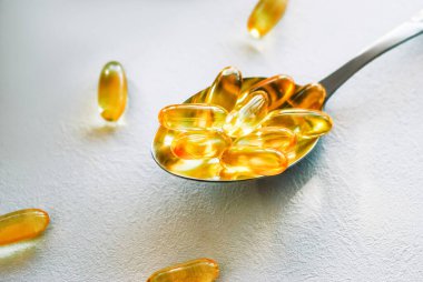 Omega 3 morina yağı içeren yemek kaşığı beyaz bir masa üstünde fotokopi alanı olan kapsüller.