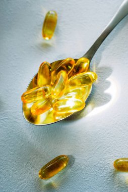 Omega 3 morina yağı içeren yemek kaşığı beyaz bir masa üstünde fotokopi alanı olan kapsüller.