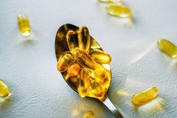 Tablespoon holding omega 3 cod liver oil supplement capsules on a white table top with copy space