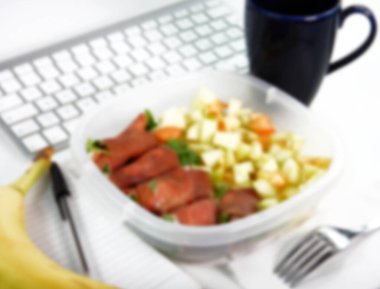 İş yerinde ev yapımı öğle yemeği (ofis): dolmalık salata, muz ve bir fincan kahve ile jambon rulosu. Bokeh etkisi için kasıtlı olarak bulanık post prodüksiyon.