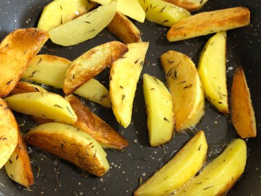 Sarı patates parçaları, zeytinyağı ve kekik ile birlikte, siyah çubuksuz tencerede..