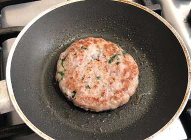 Yağlı siyah bir tencerede küçük bir hamburger pişirmek..