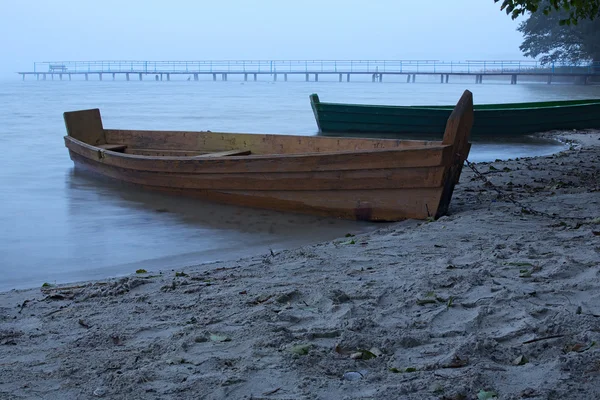 Nebliger Morgen auf dem See. zwei Boote am Ufer in der Nähe der alten verlassenen Seebrücke — Stockfoto