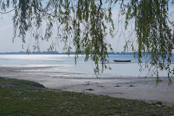 Se puede ver el lago detrás de las ramas. Barco pesquero de madera amarrado cerca de la orilla —  Fotos de Stock