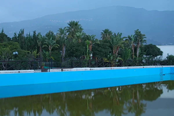 Es gibt einen kleinen Park mit verschiedenen Bäumen hinter dem Pool. im Hintergrund Berge im Nebel. Marina di Patti. Sizilien — Stockfoto