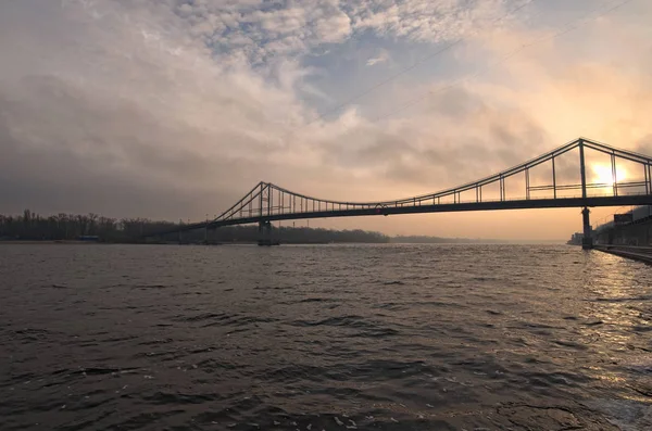 Gångbro till ön Trukhanov i Kiev genom floden Dnipro i soluppgången. Vintermorgon. Ukraina. Selektivt fokus med vidvinkelobjektiv — Stockfoto