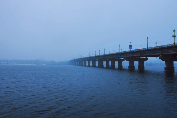 Kyiv winter cityscape with Paton bridge over Dnieper river. Foggy morning view. A few minutes before the snowfall