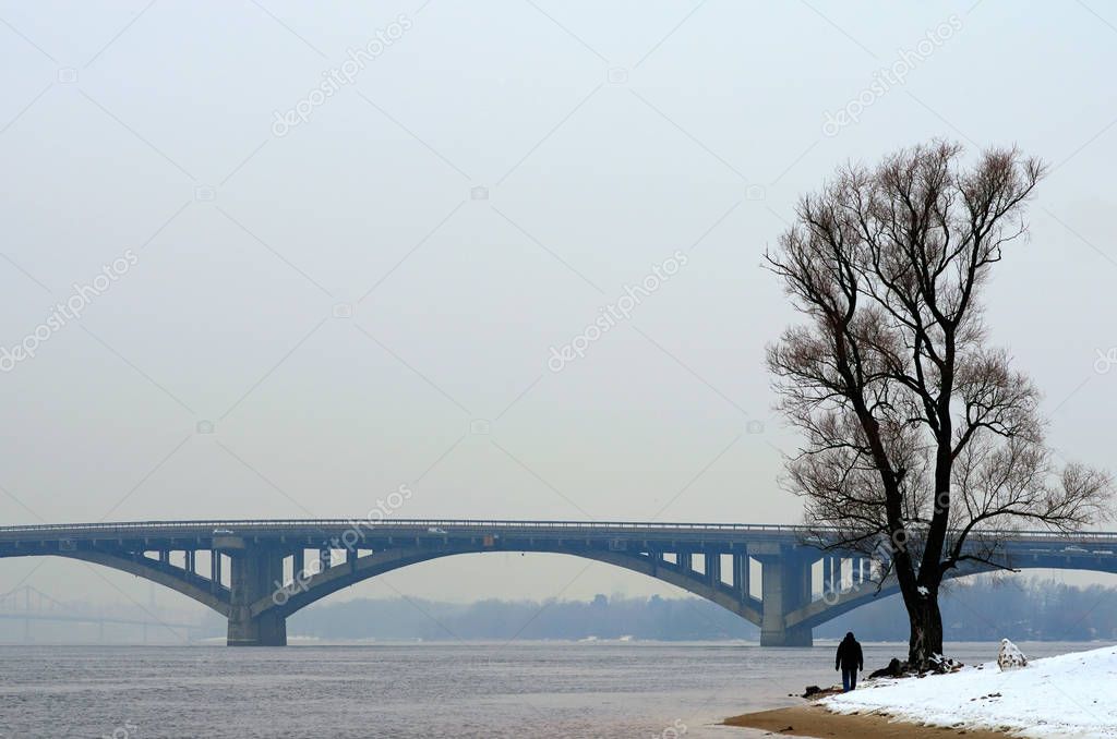 One man is walking along the bank of the Dnieper River. Winter landscape photo. Kyiv, Ukraine