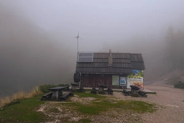 Vrsic Pass, Słowenia-25 września 2019: Tajemnicze zdjęcie krajobrazowe Vrsic Pass. Zamknięta kawiarnia na świeżym powietrzu z drewnianymi stołami i ławkami. Gęsta mgła kryje góry. — Zdjęcie stockowe