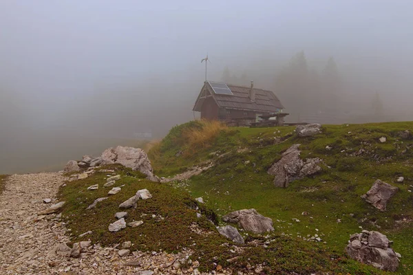 Tajemnicze zdjęcie krajobrazowe przełęczy Vrsic. Zamknięta kawiarnia na świeżym powietrzu z drewnianymi stołami i ławkami w tle. Gęsta mgła kryje góry. — Zdjęcie stockowe