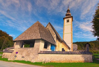 Bohinj Gölü yakınlarındaki John the Baptist Kilisesi 'nin geniş açılı manzara manzarası canlı mavi gökyüzüne karşı. Güneşli bir sonbahar günü. Triglav Ulusal Parkı, Slovenya. Ünlü turistik yer ve romantik seyahat merkezi.