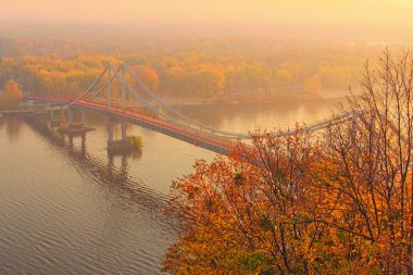 Ünlü Dnipro Nehri 'nin sonbahar manzarası. Yaya köprüsü suya yansıdı. Arka planda sonbahar renkleri olan doğa manzarası. Kyiv, Ukrayna