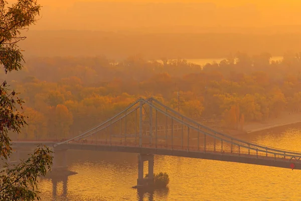 Aerial morning view of Dnieper River and Pedestrian Bridge. Foggy weather with orange sky during sunrise. Autumn colors in the background. Romantic and peaceful scene. Kyiv, Ukraine — Stock Photo, Image