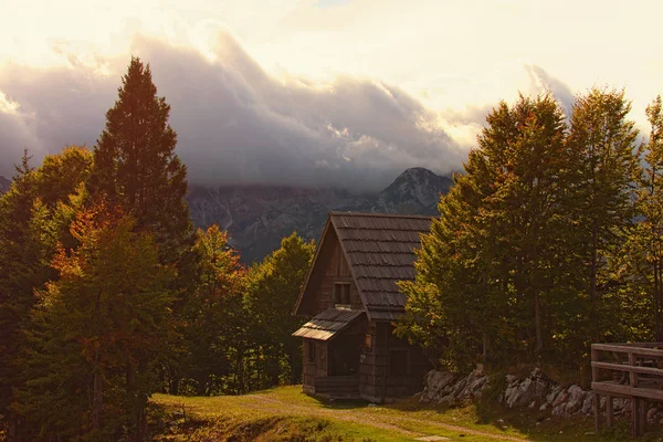 Magic mountain autumn landscape. Wooden shelter in the autumn color forest. High mountain peaks with thunderclouds. Dramatic scene. Concept of landscape and nature. Vogel ski center, Slovenia