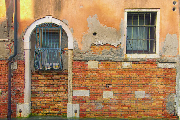 Ancient red brick wall with two windows. Canal with turquoise water flows under the wall. Venice, Italy
