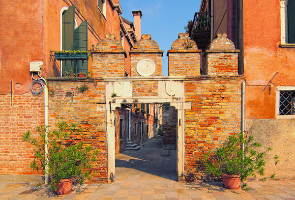 Picturesque city landscape of Venice. Medieval facade of red brick building and gate door. Non-tourist part of the city. Famous touristic place and travel destination in Europe. Venice, Italy.