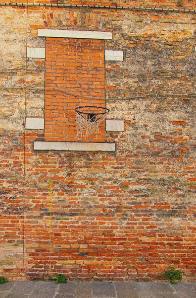 Cour de rue avec un vieux panier de basket sur le mur de briques rouges. La fenêtre est murée par la brique. Venise, Italie — Photo