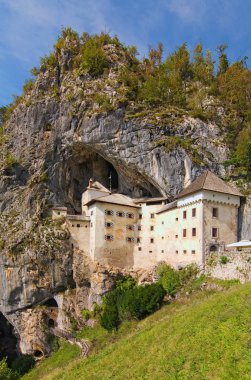 Mağaradaki ortaçağ şatosunun resimli manzarası. Ünlü Predjama kalesi (Slovene. Predjamski mezunu). Slovenya 'da popüler bir seyahat merkezi. Güneşli bir sonbahar günü. Slovenya 'nın Predjama Köyü
