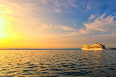 Büyük, beyaz bir yolcu gemisinin muhteşem manzarası. Panoramik dramatik günbatımı gökyüzü. Gemi Koper limanından çıkıyor. Seyahat ve turizm konsepti. Koper, Slovenya