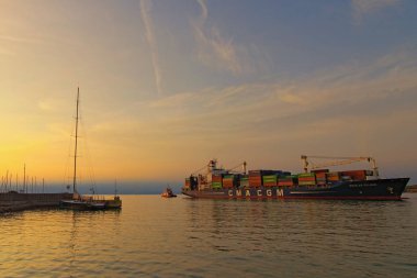 Koper, Slovenya-27 Eylül 2019: Römorkör büyük konteynır gemisini limandan çıkardı. İthalat, ihracat ve iş lojistiği. Uluslararası su taşımacılığı. Gün batımında güzel manzara