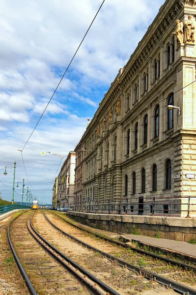 Budapest, 01.10.2019: Schienen für Straßenbahnen am Donauufer. Im Hintergrund die typische gelbe Straßenbahn. 2. Mittelalterliche Gebäude auf der rechten Seite — Stockfoto