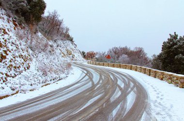 Kardan sonra dramatik kış manzarası. Dağlarda ve ormandaki karla kaplı ağaçlarda resim gibi virajlı bir yol. Meteora, Yunanistan