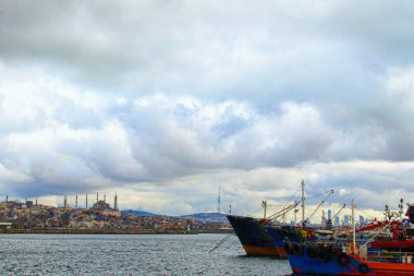 İstanbul 'da demirli balıkçı tekneleri ve gemileriyle liman manzarası. Arka planda şehir manzarası. Dramatik kış gökyüzü. İstanbul, Türkiye