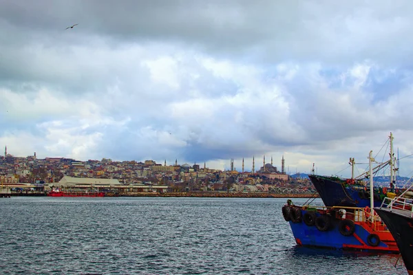 İstanbul 'da demirli balıkçı tekneleri ve gemileriyle liman manzarası. Arka planda şehir manzarası. Dramatik kış gökyüzü. İstanbul, Türkiye