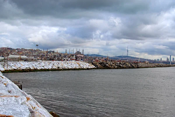 Kamením zpevněné pobřeží v Istanbulu proti dramatickému nebi. Přístav s rybářskými čluny a loděmi ve městě. Městská krajina v pozadí. Zimní krajina. Turecko, Istanbul — Stock fotografie