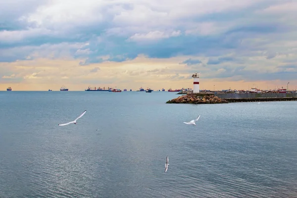 Farol branco no final do cais com equipamento de navegação especial indica a entrada do porto. Barco de pesca solitário no mar. Céu nebuloso dramático. Istambul, Turquia — Fotografia de Stock