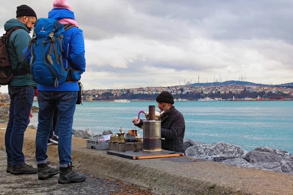 Istanbul, Turkey-January 03, 2020: A local man makes turkish coffee for tourists. Embankment of Bosphorus. Concept of small business, street food. Silhouette of Istanbul in the background — Stock Photo, Image