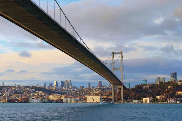 Bottom view of Bosphorus Bridge (also known as 15 July Martyrs Bridge) over strait. Beylerbeyi district with Beylerbeyi Mosque in the background. Beautiful landscape on a winter sunny day — 스톡 사진