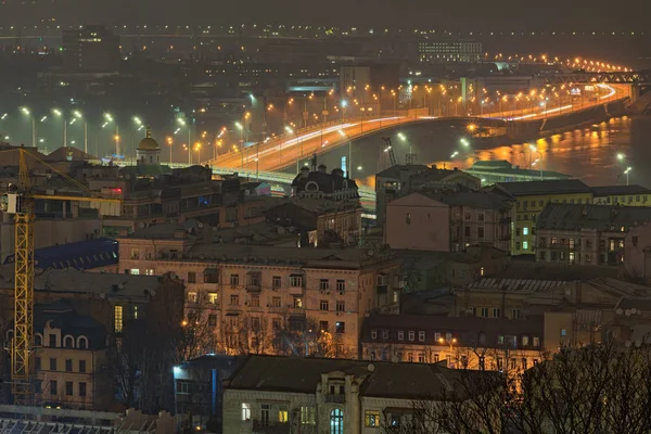 Hermoso paisaje iluminado noche de Podil. Es uno de los barrios más antiguos de Kiev. Se encuentra cerca del río Dnipro. Techos de edificios antiguos y puente del puerto en el fondo. Ucrania — Foto de Stock