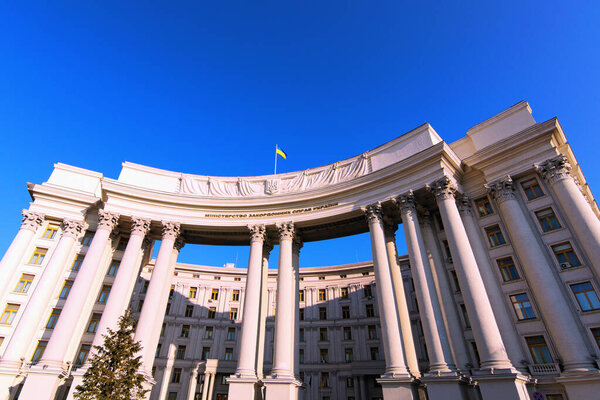 Wide-angle landscape view of building with columns of Ministry of Foreign Affairs of Ukraine against blue sky. Ukrainian Trident is coat of arms, Flag of the Ukraine on the top of the building.