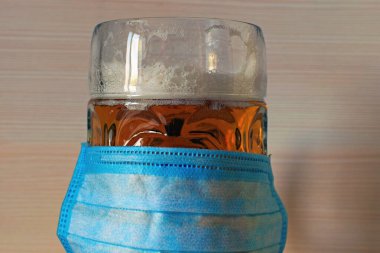 Antivirüs (Coronavirus, COVID-19) reklam konsepti. Mavi antivirüs maskesinin yakından görüntüsü 1 litrelik bardakta, adı Mab ve bira. Soyut tahta arkaplan. 