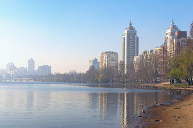 Dinyeper Nehri manzarası ve modern Obolon bölgesindeki boş plaj manzarası. Arka planda sabah sisli gökdelenleri olan toprak seti. Binalar suya yansıdı. Kyiv, Ukrayna.