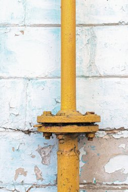 Flanj bağlantısı olan eski sarı gaz borusunun yakın görüntüsü. Soyulan duvarda beyaz bir tuğla. Soyut arkaplan.